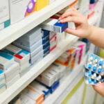 Pharmacist holding medicine box and capsule pack in pharmacy drugstore.